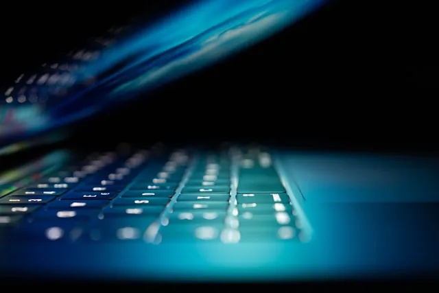 A close-up view of a partially open laptop with illuminated keys in a dark environment.