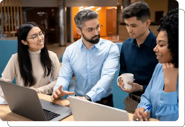 Four colleagues discussing a project over a laptop in a modern office setting.