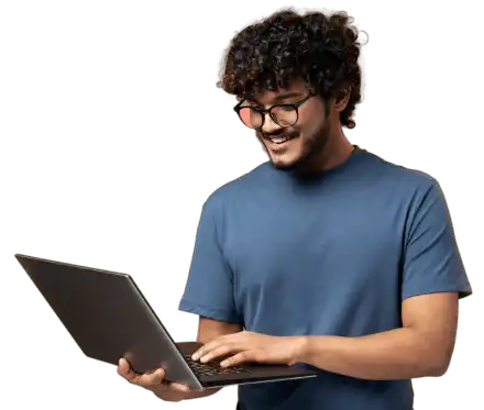 A smiling young man with curly hair and glasses using a laptop computer.